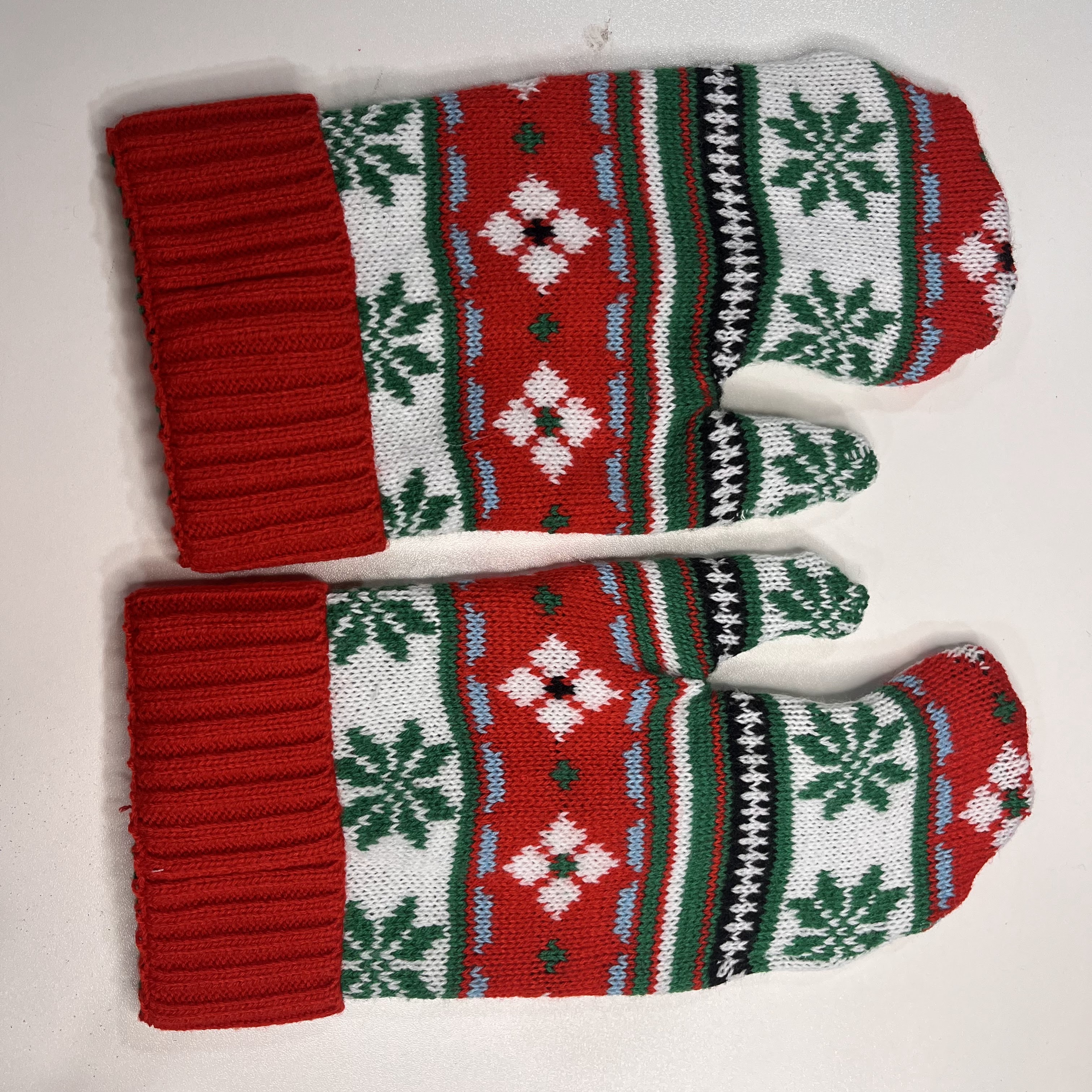 mittens made from sweater sleeves. The mittens are red white and green with green snowflakes and white diamond shapes. There are small accents of blue and black.